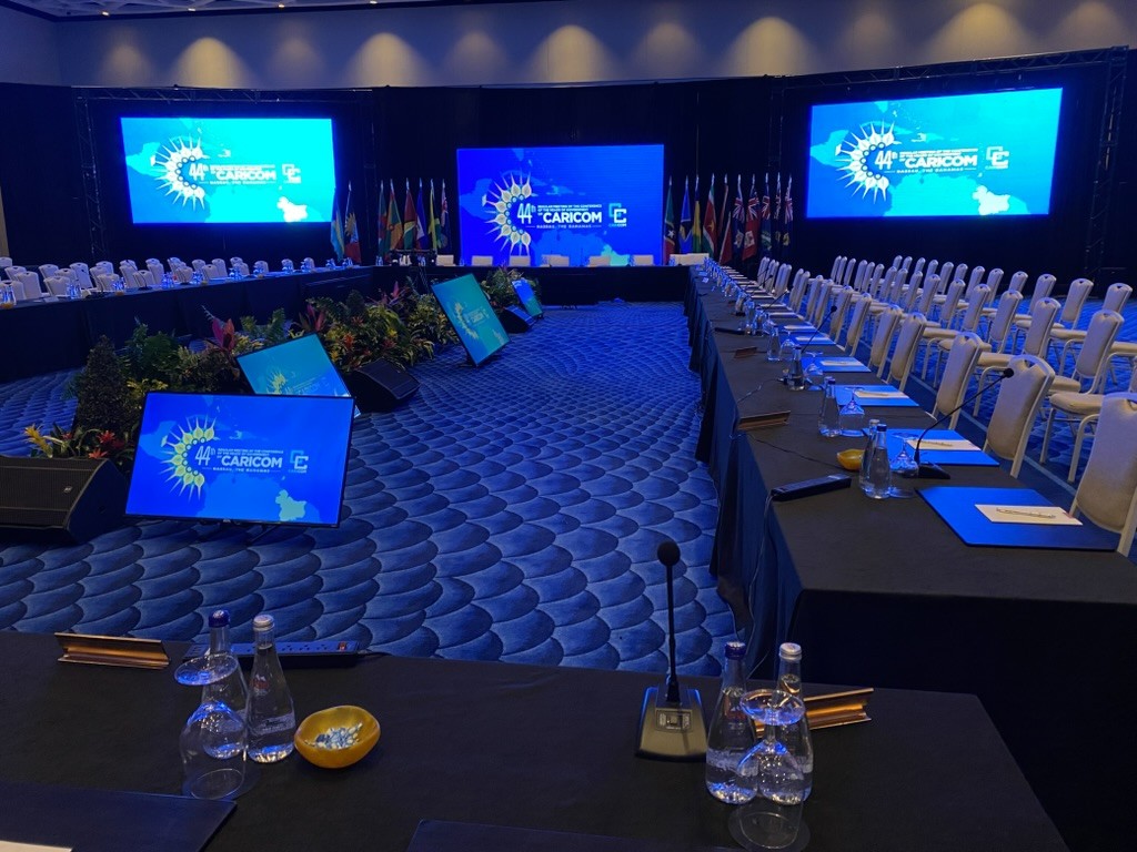 Large conference room set for the 44th CARICOM meeting with long tables, microphones, and event-branded screens.