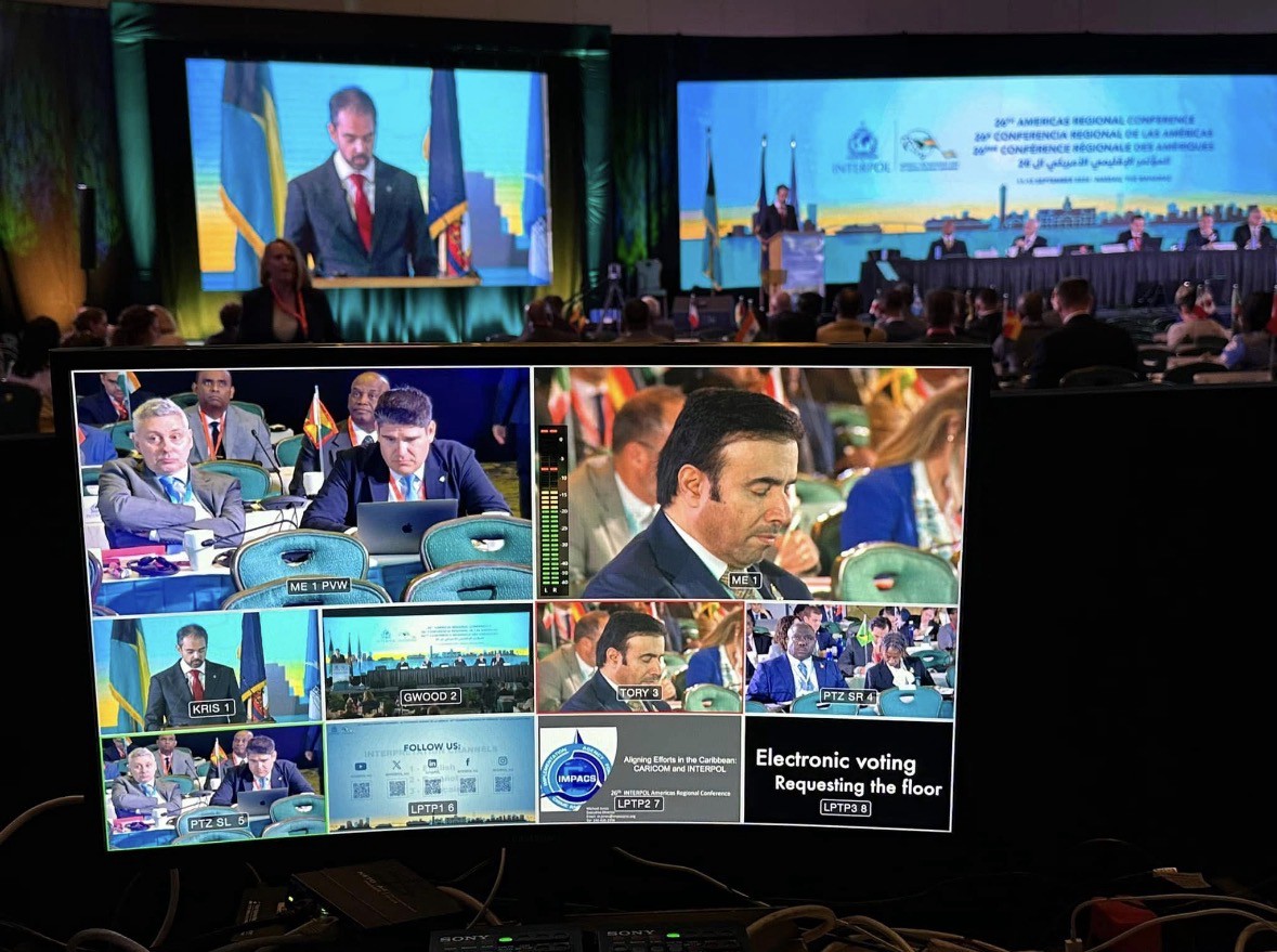 Multi-view monitor showing a live video production grid for an INTERPOL conference with camera angles, slides, and audio levels.
